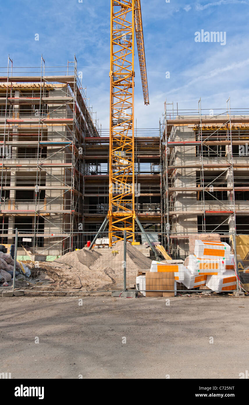 Large construction site with scaffolding building, yellow tower crane and clear blue sky. Stock Photo
