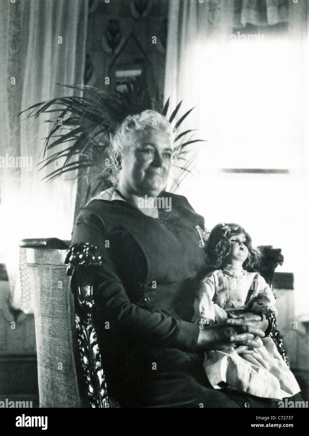 An older Portuguese lady from the island of Pico in the Azores, sits, with a doll, in a chair with carved wooden lion heads Stock Photo