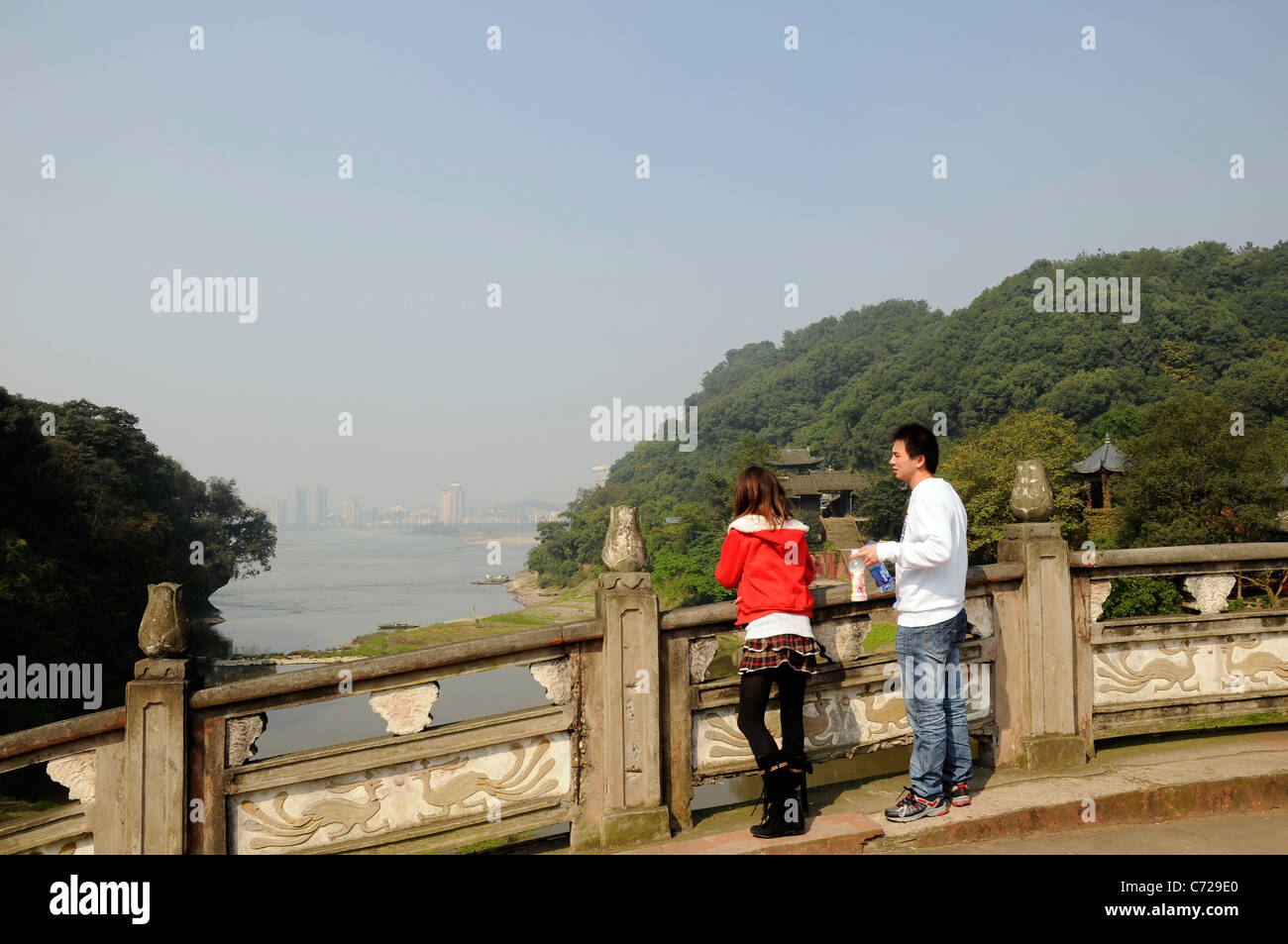 A couple of young Chinese tourists looking out towards a city in the distance. Dafo, Leshan, China. Showing pollution in the air Stock Photo