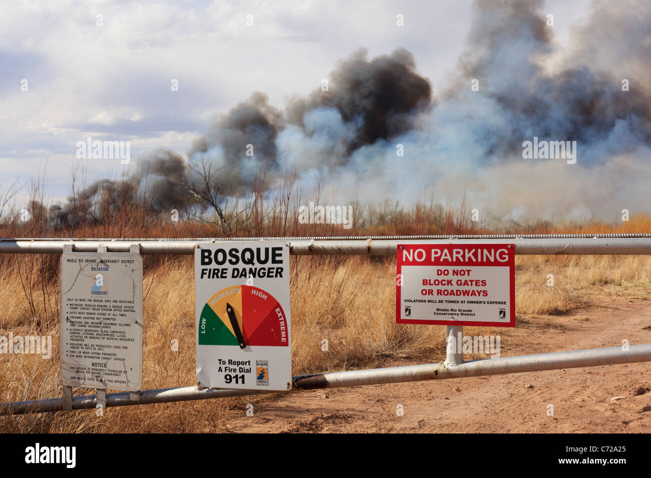 A fire danger sign and gate in rural New Mexico with wildfire burning in the background. Stock Photo