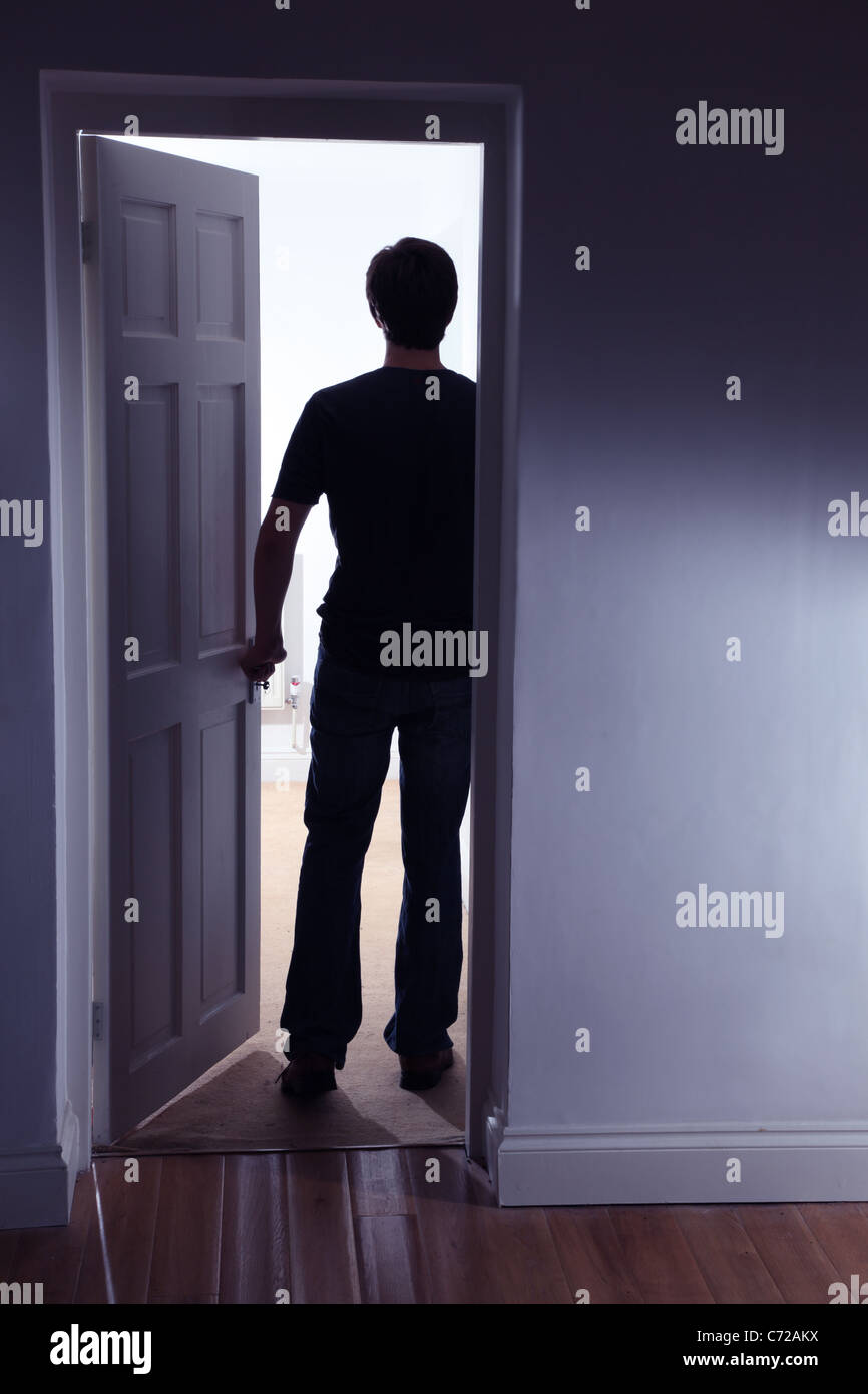 Back view of a male figure entering a well lit room leaving a dark room Stock Photo