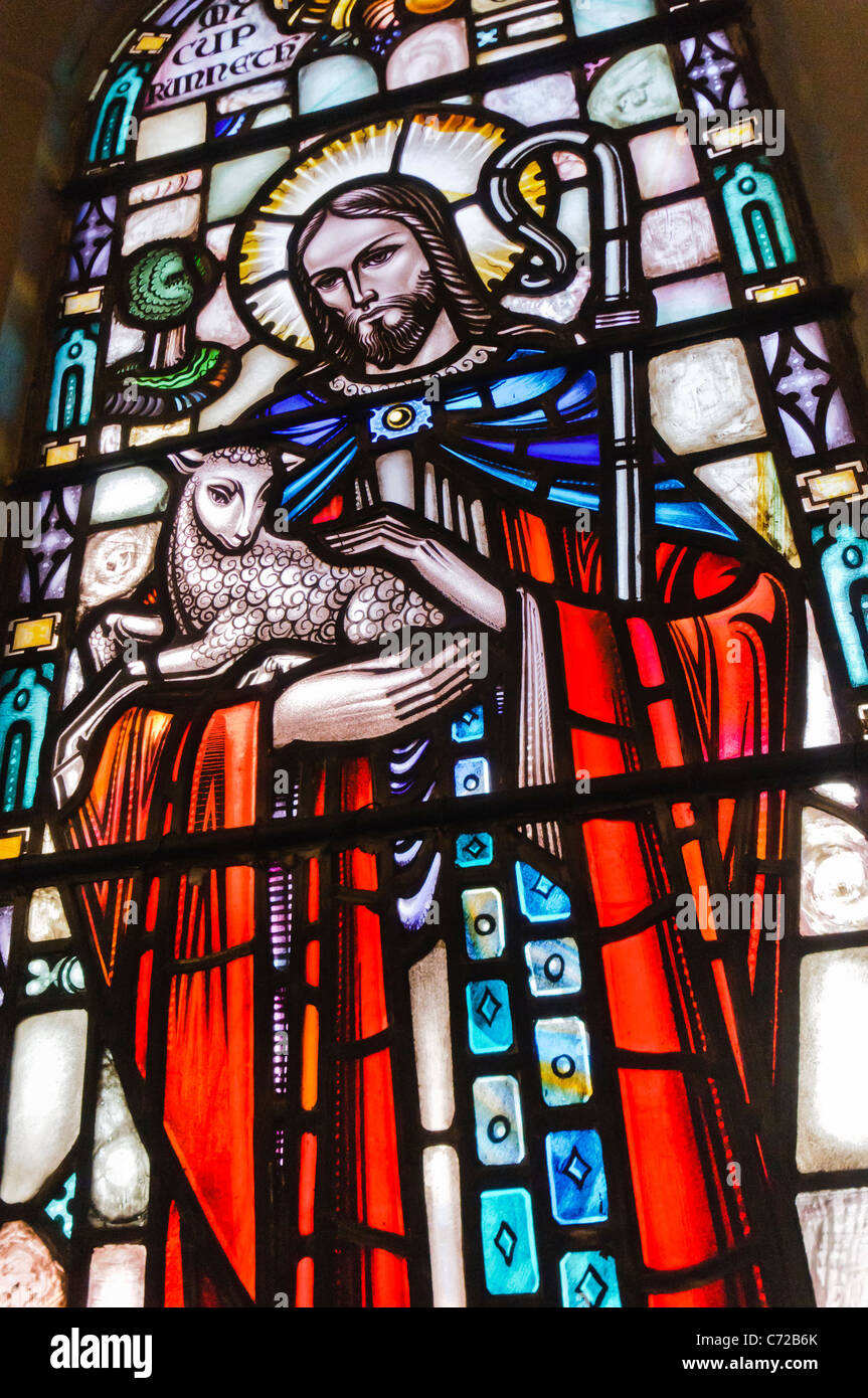 Stained glass window in a church showing Jesus holding a lamb and depicted as a shepherd tending his flock. Stock Photo