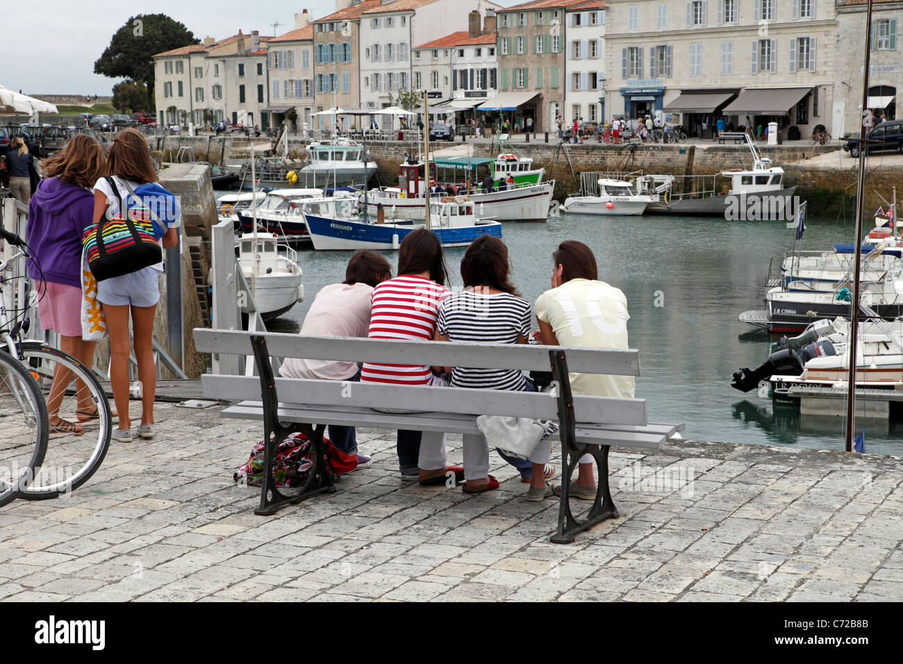 Young ladies chatting on a bench Ile de Re harbour St Martin Stock Photo