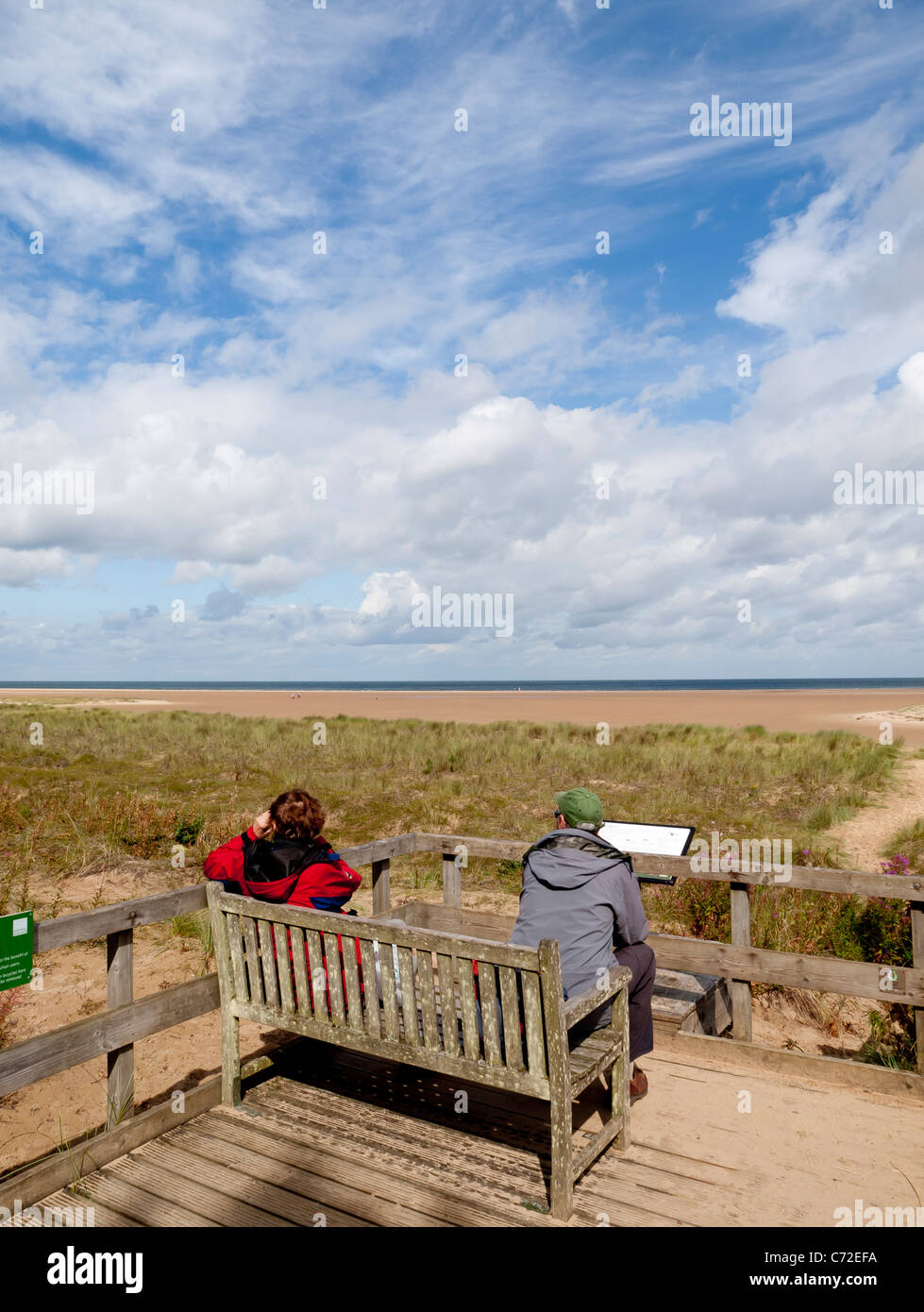 A couple rest on a bench at Holkham Beach look out point Norfolk UK Stock Photo