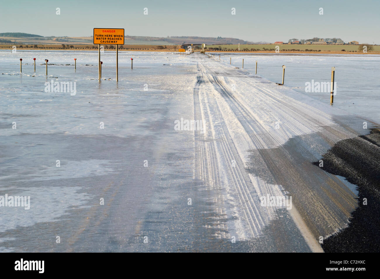 The tidal causeway road leading to Lindisfarne (Holy) Island, with the mudflats covered by ice. Stock Photo