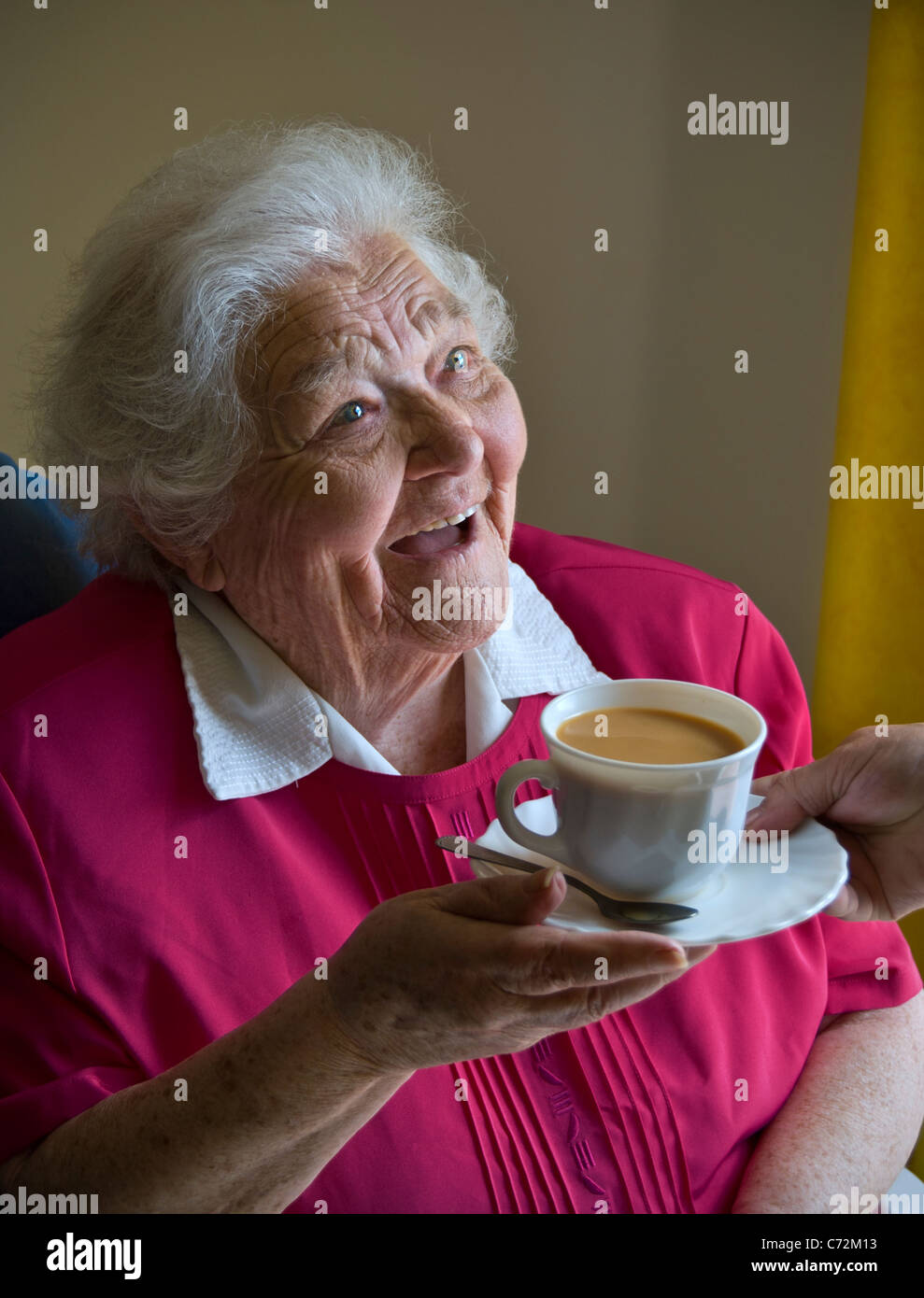 Elderly tea care carer happy alert senior old age pensioner old  elderly lady receives a cup of tea from carer caring companion in her light airy room Stock Photo