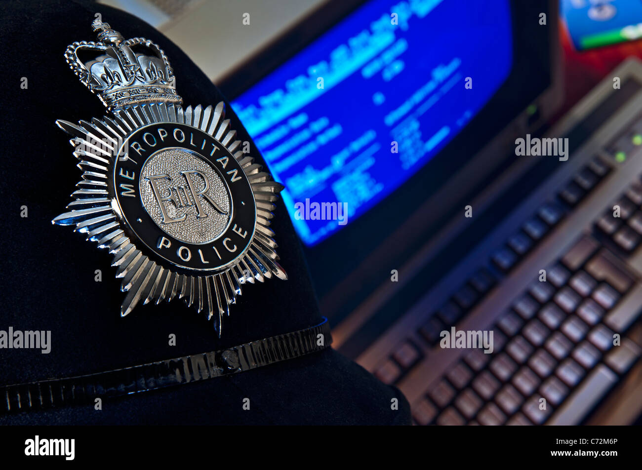 Concept Metropolitan police helmet and badge with computer screen in background Stock Photo