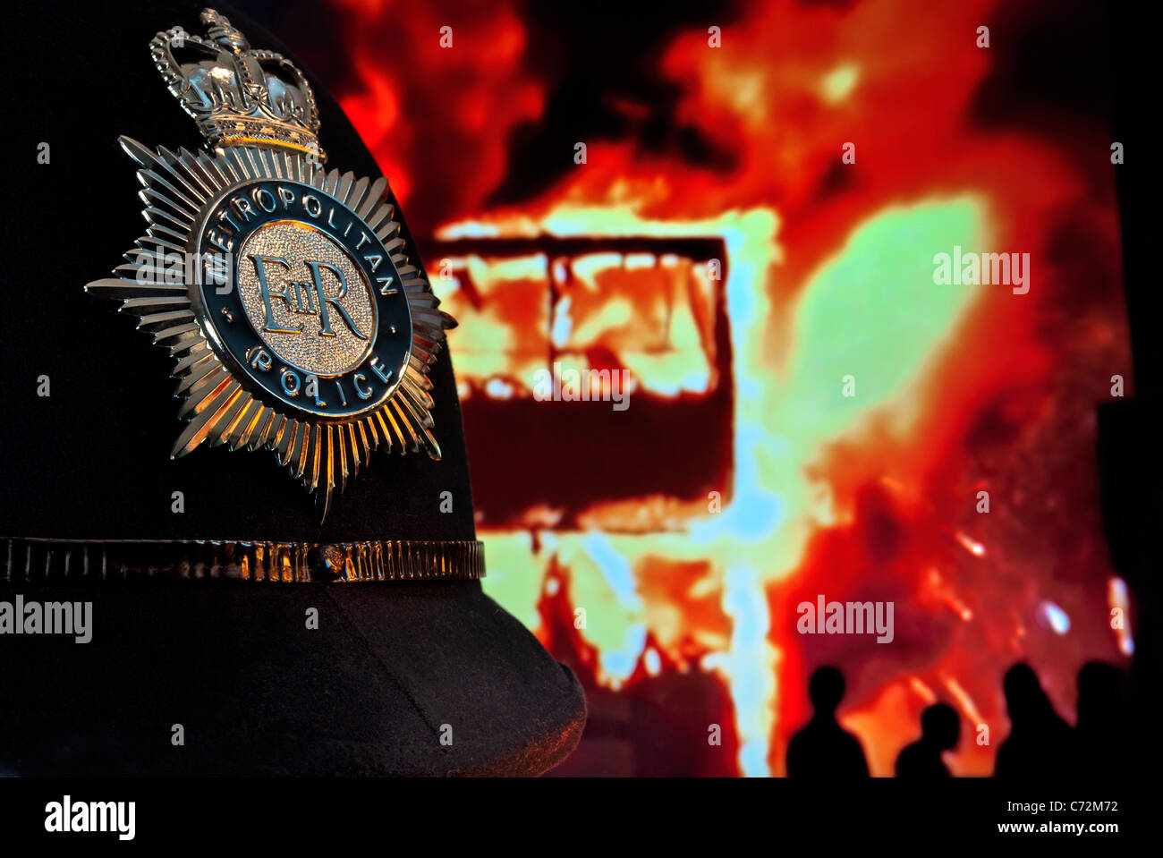 Metropolitan police helmet and badge with rioters and London bus in flames behind Stock Photo