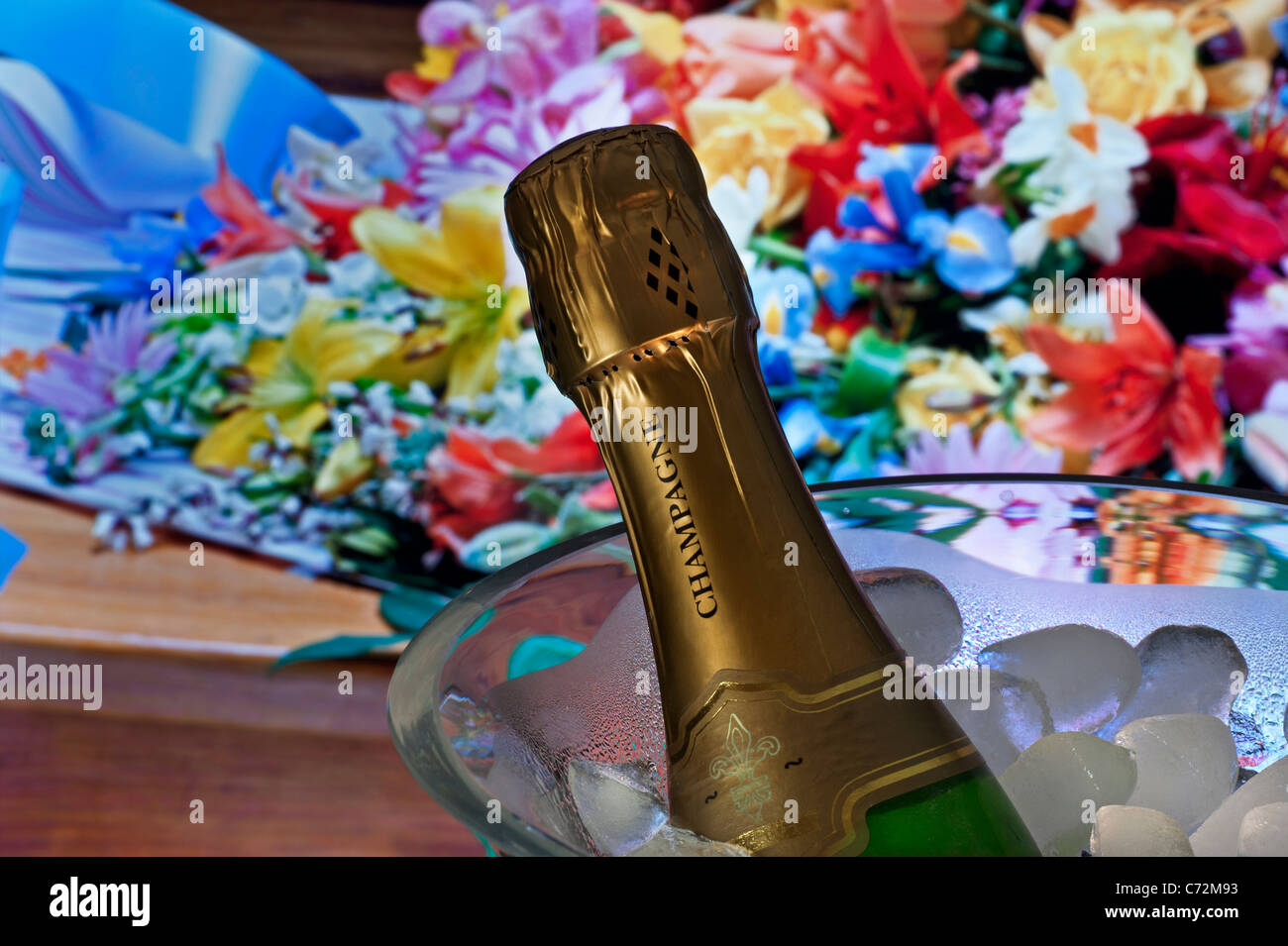 Champagne bottle on ice in wine cooler with bouquet selection of flowers on table behind Stock Photo