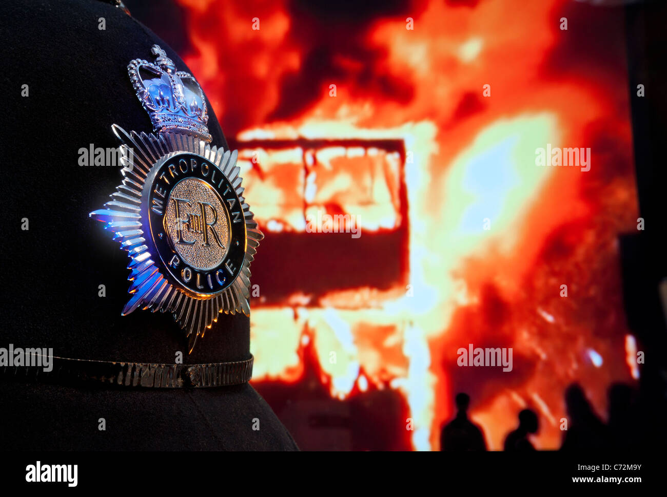 London riots Met police helmet & badge with fire flames rioters London bus in flames behind. Looting Riots London lawless streets Police Arrest Stock Photo