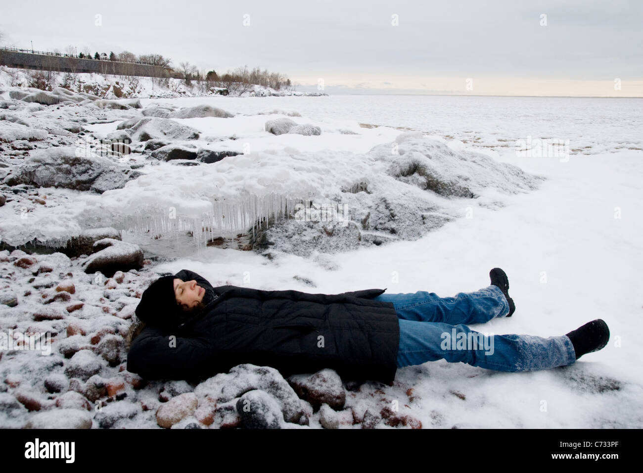 A woman lying on a rocky, icy, beach. Stock Photo