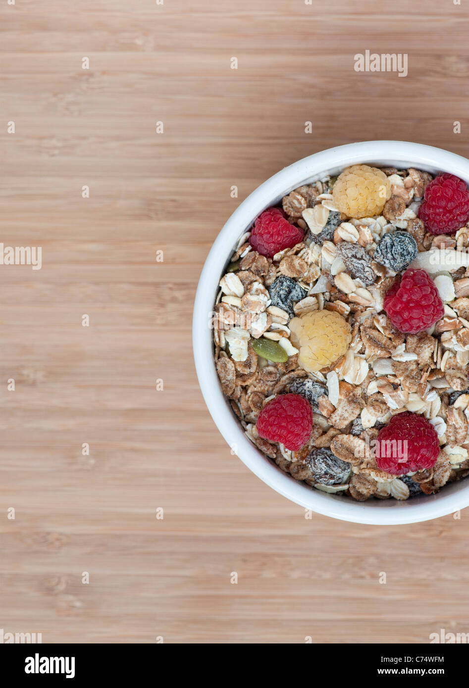 Muesli and fresh raspberries in a bowl on a bamboo wood board. From above side of frame Stock Photo