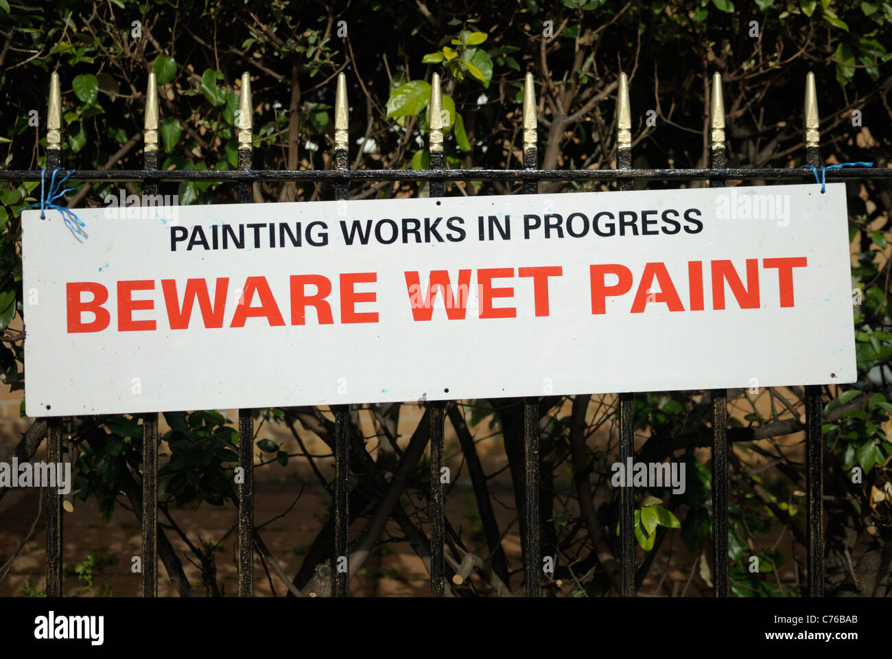 A 'Beware Wet Paint' sign attached/tied to some metal railings. Stock Photo
