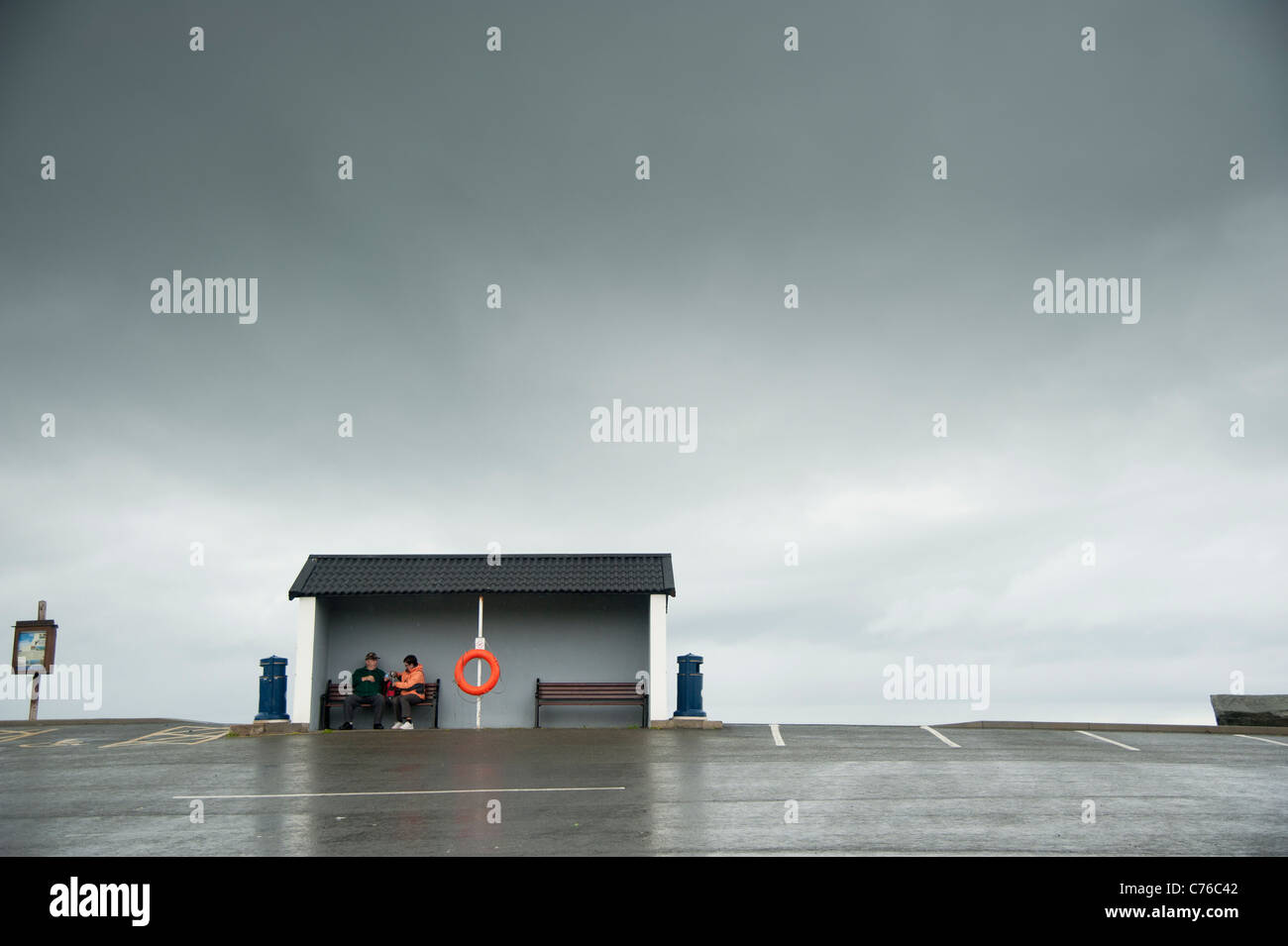 two people sheltering from the rain on a grey overcast rainy wet afternoon, Aberaeron Wales UK Stock Photo