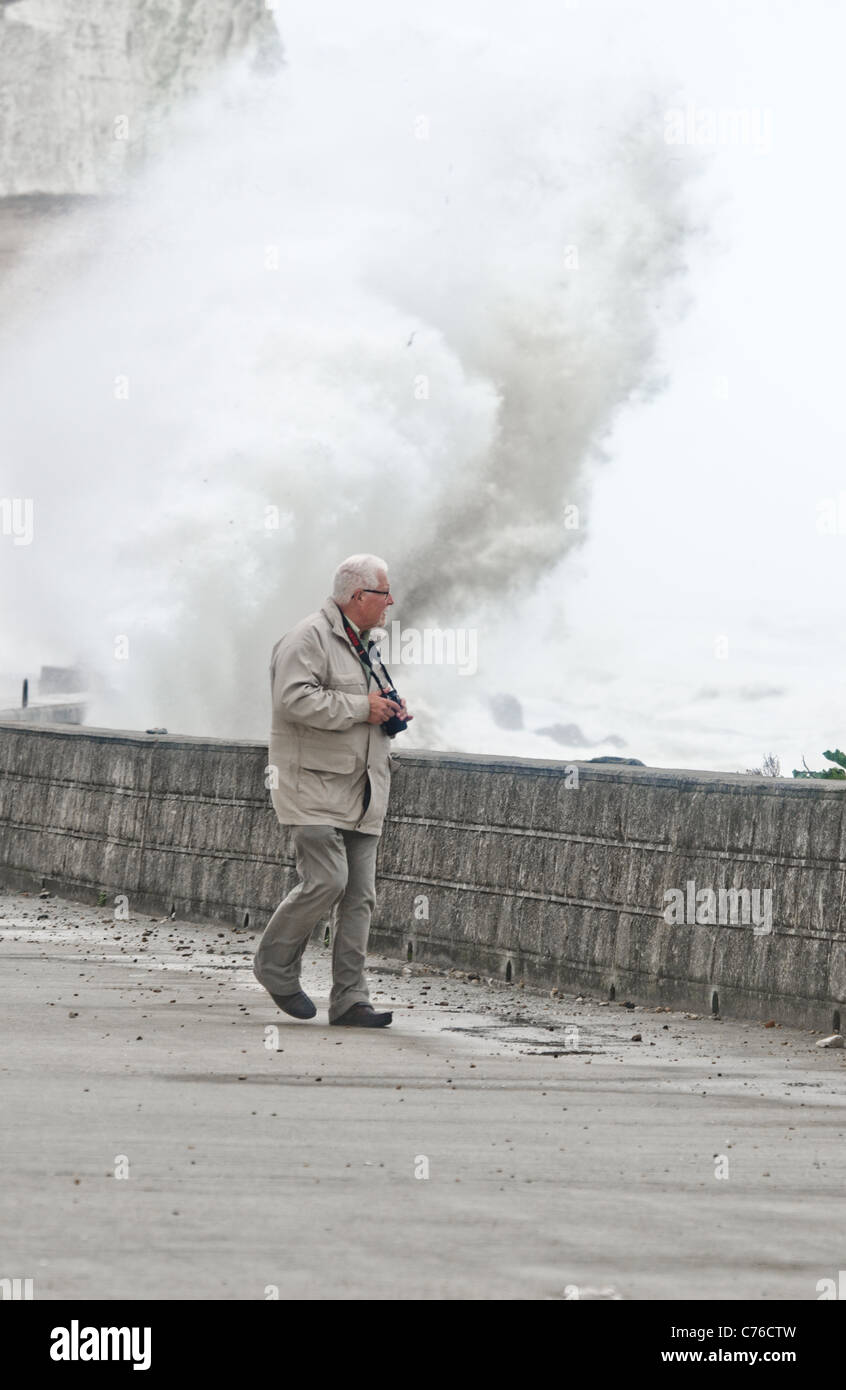 bad weather as man walks on sea defenses promenade and waves crash against the shore Stock Photo