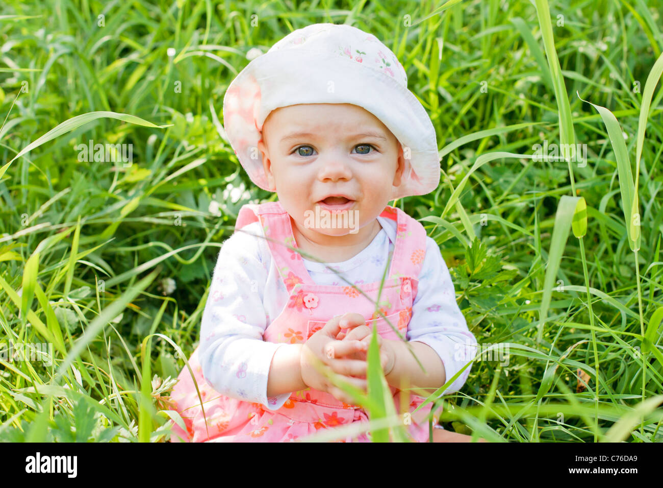 Happy baby girl with blue eyes lying on grass Stock Photo