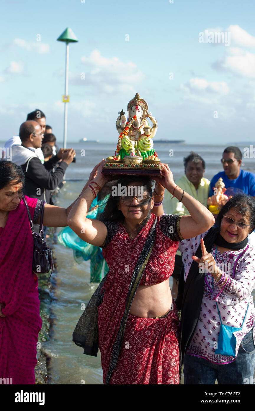 Hindu woman carries a statue of Lord Ganesh on her head into the sea at the Ganesh Festival in Essex. Photo:Simon Ford Stock Photo