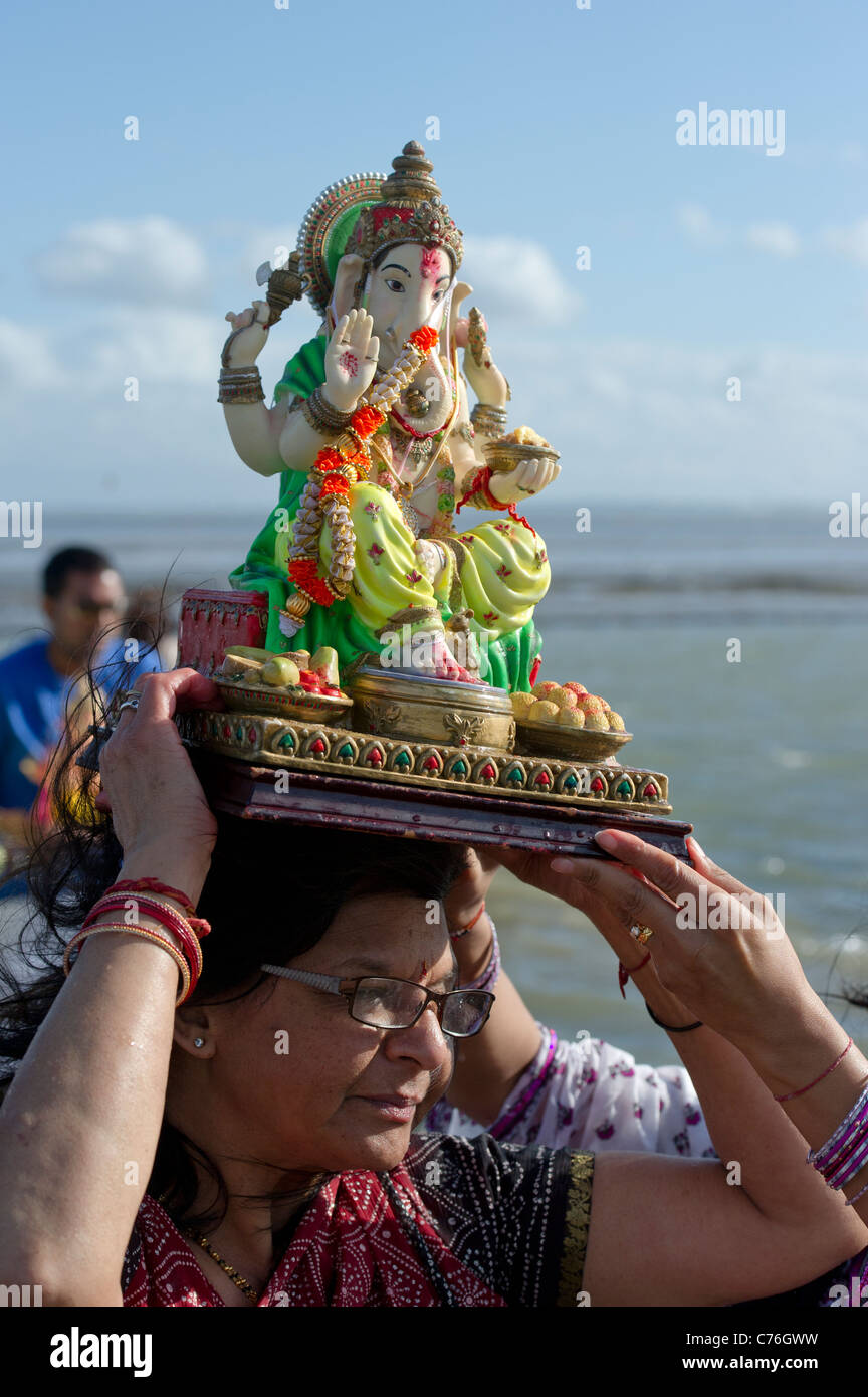 Hindu woman carries a statue of Lord Ganesh on her head into the sea at the Ganesh Festival in Essex. Photo:Simon Ford Stock Photo