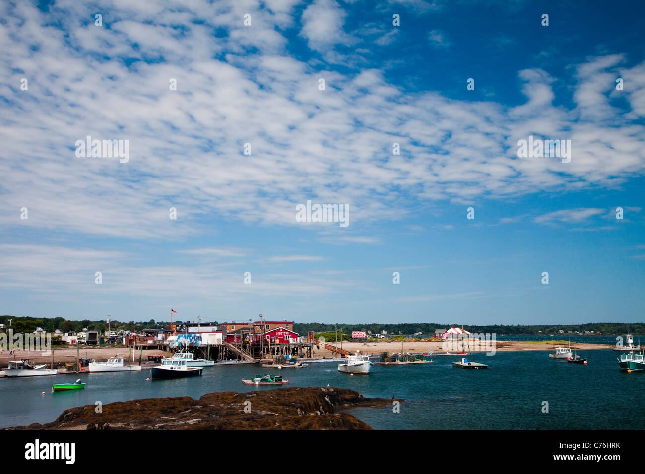 A red building on the edge of a small harbor with boats floating on a sunny day. Stock Photo