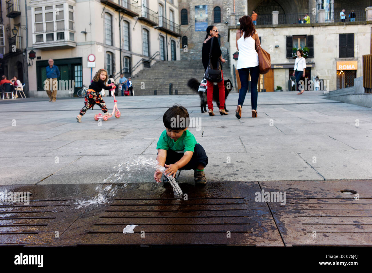 A mixed race toddler plays with fountain in a plaza in the basque ...