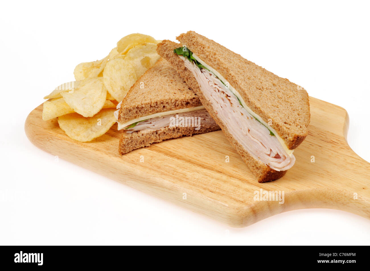 Turkey and cheese sandwich on whole meal bread cut in half  with crisps on wood cutting board on white background. Stock Photo
