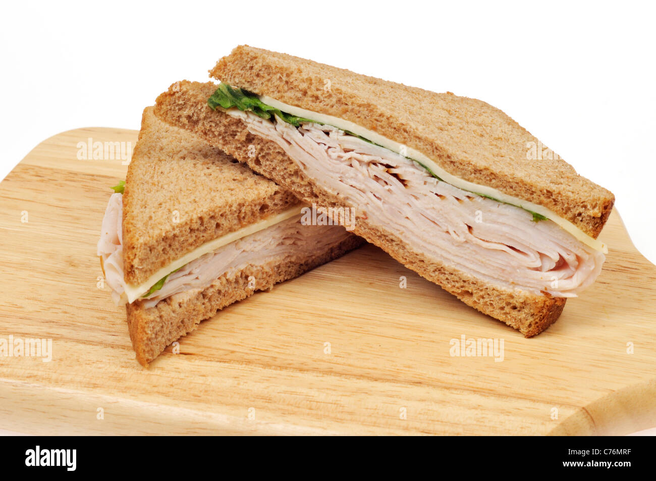 Turkey and cheese sandwich on whole meal bread cut in half on wood cutting board on white background. Stock Photo