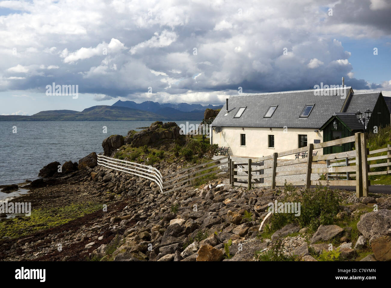 Sunlit white cottage at Ord on the Isle of Skye with Loch Eishort and Cuillin Mountains beyond