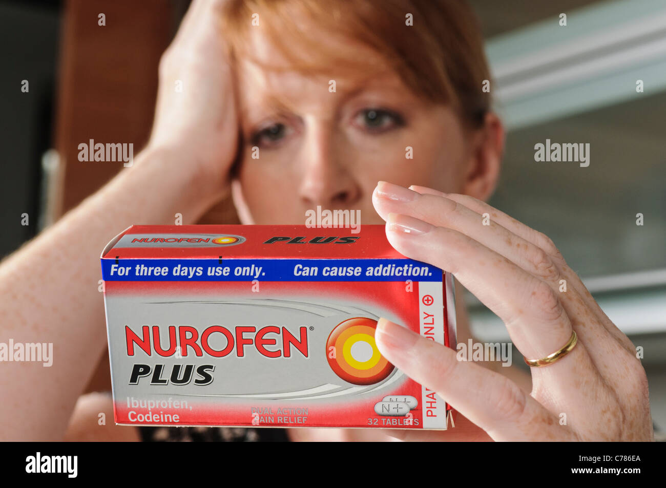 Woman with headache reads the back of a box of 32 Nurofen Plus tablets Stock Photo