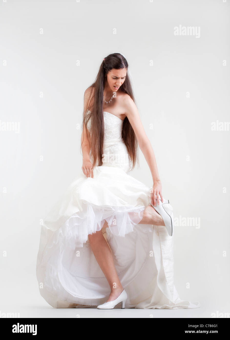 bride in wedding dress taking off her shoe checking her hurting foot Stock Photo