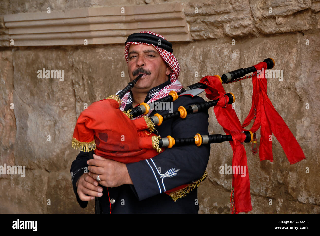 Jordanian bagpiper with a red bagpipe against a wall. Stock Photo