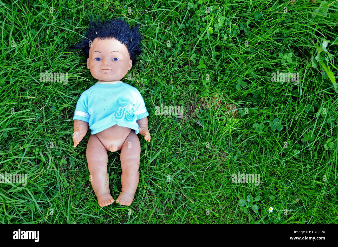 Plastic ethnic male doll abandoned thrown away on grass Stock Photo