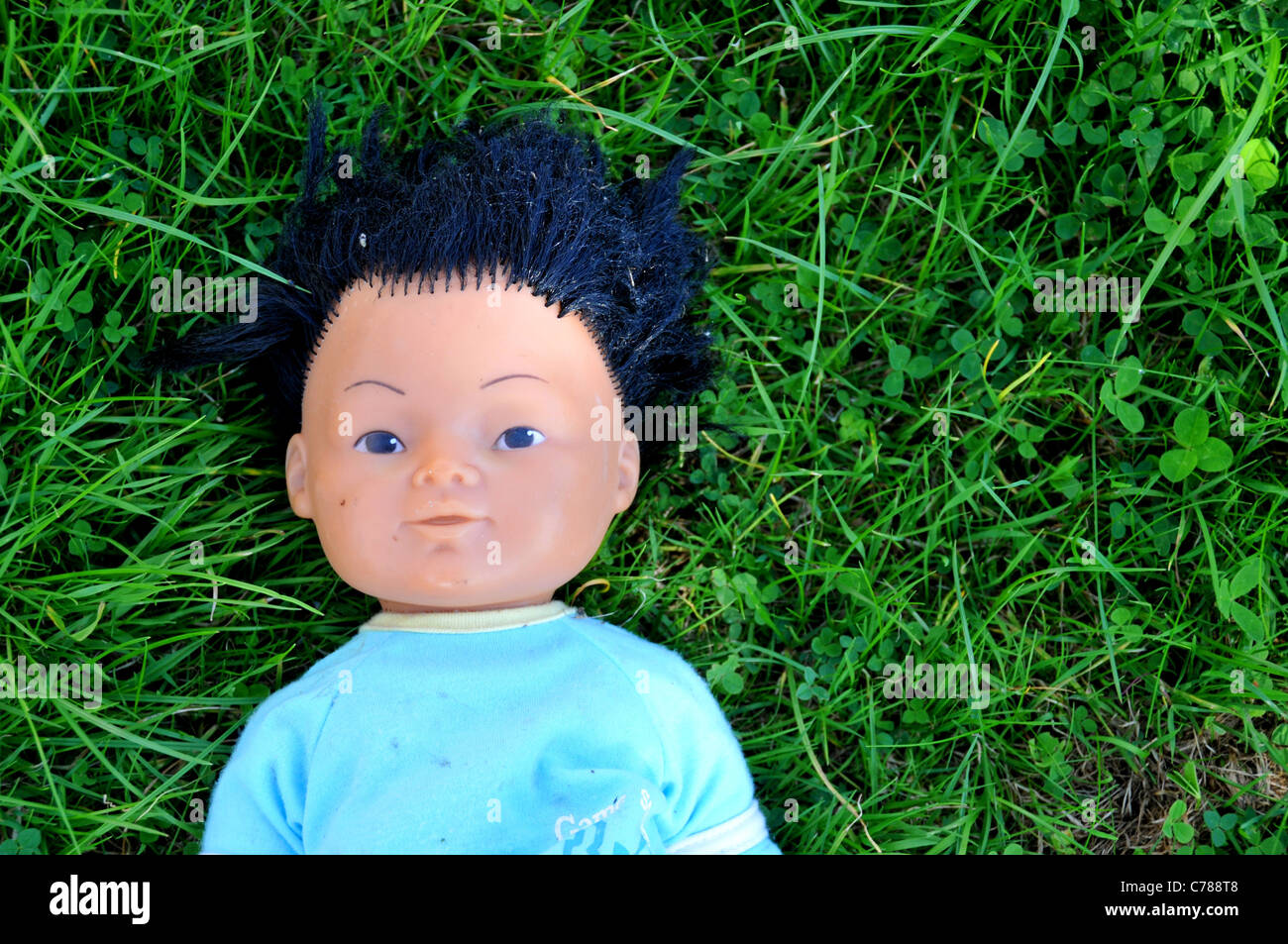 Plastic ethnic male doll abandoned thrown away on grass Stock Photo