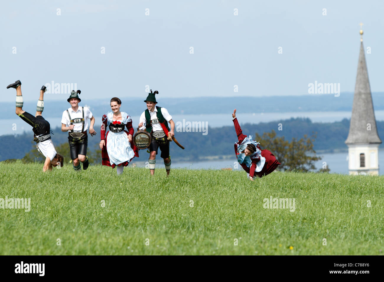 Young people running and somersaulting on a field of grass in traditional Bavarian costumes, Hittenkirchen Chiemgau Upper Bavari Stock Photo