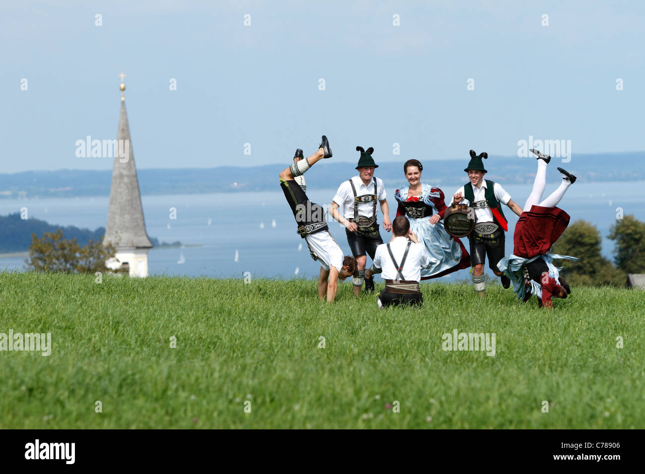 Young Bavarians being photographed while running and somersaulting on a field of grass in traditional Bavarian costumes, Hittenk Stock Photo