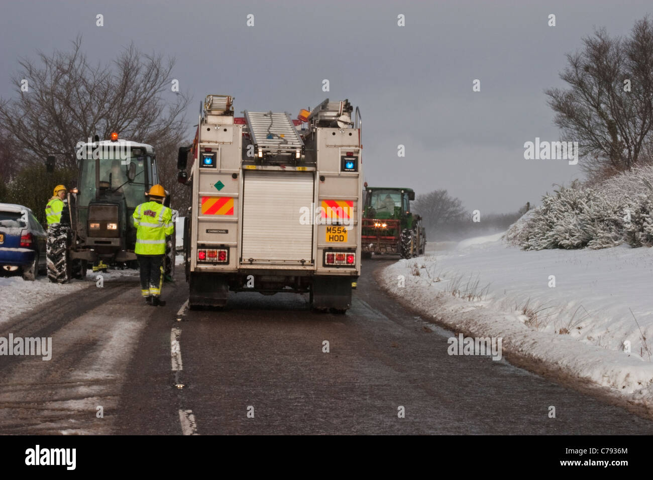Trunk-road blocked in heavy snow after a vehicle went off the road. Local tractors and fire crew assist. Stock Photo
