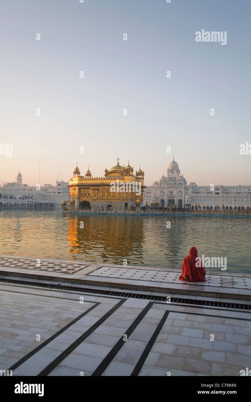 A woman sits at dawn by the side of the lake in which sits the Sikh Golden Temple in Amritsar, India, Punjab state Stock Photo
