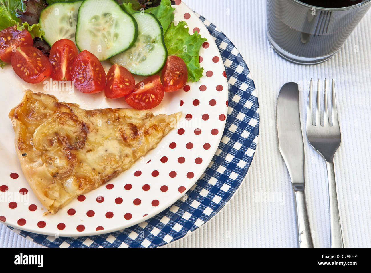 An onion-cheese tart, garnished with a salad and a glass of red wine Stock Photo