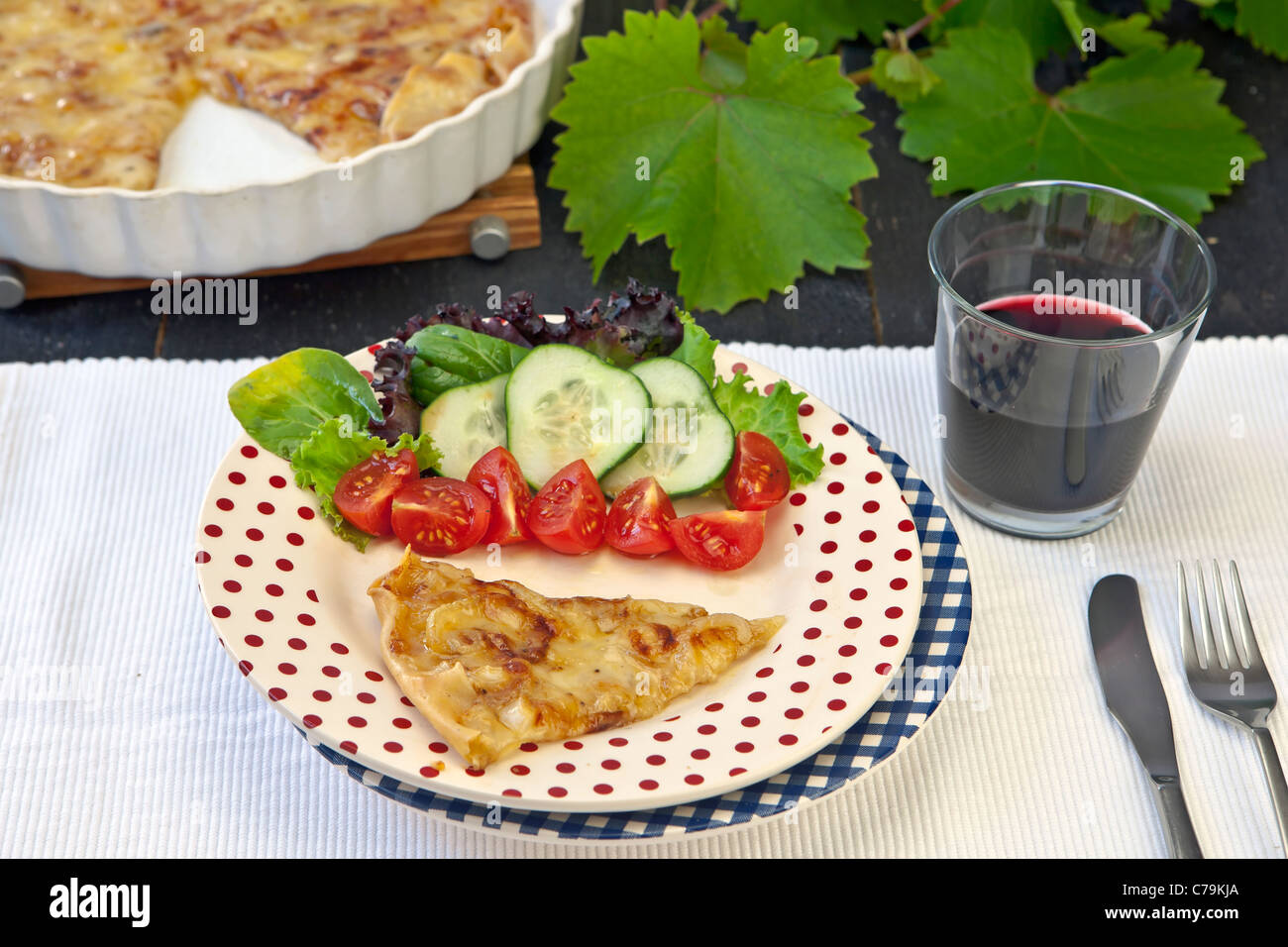 An onion-cheese tart, garnished with a salad and a glass of red wine Stock Photo