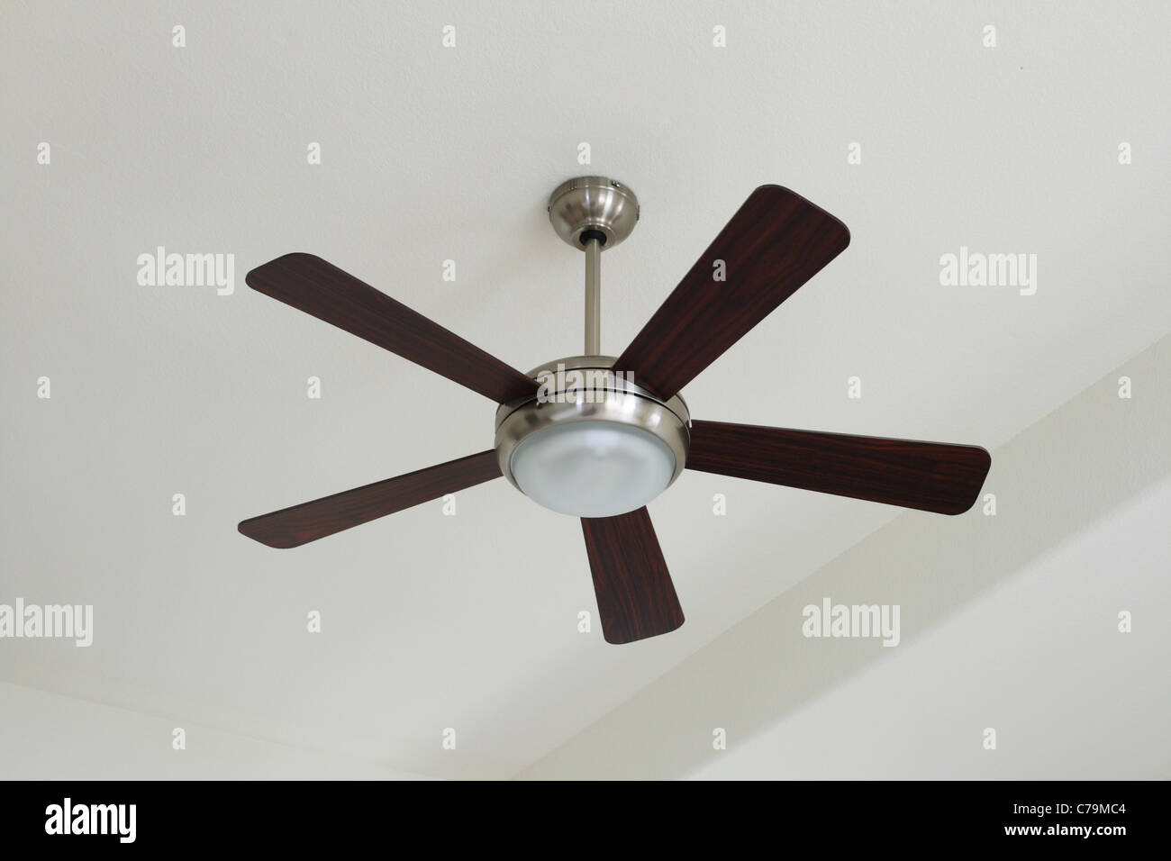silver and wood ceiling fan with a light on a white ceiling Stock Photo