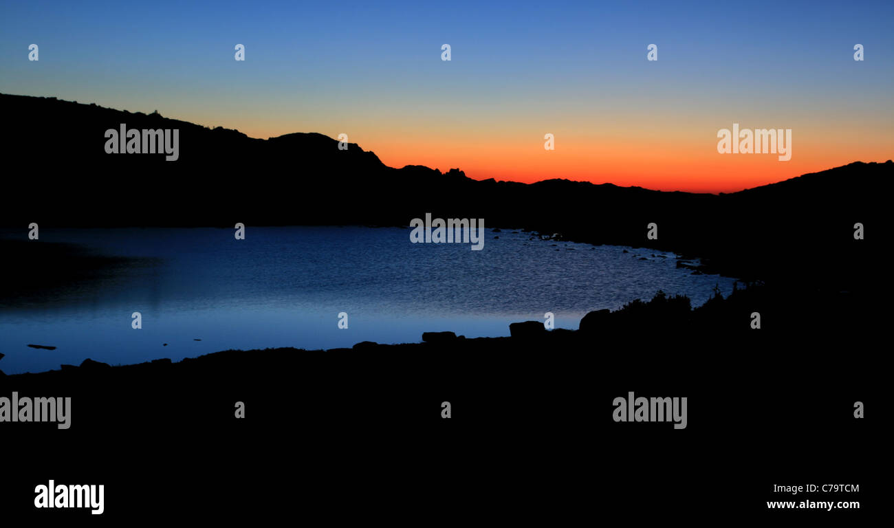 before sunrise the sky turns reddish over an alpine lake Stock Photo