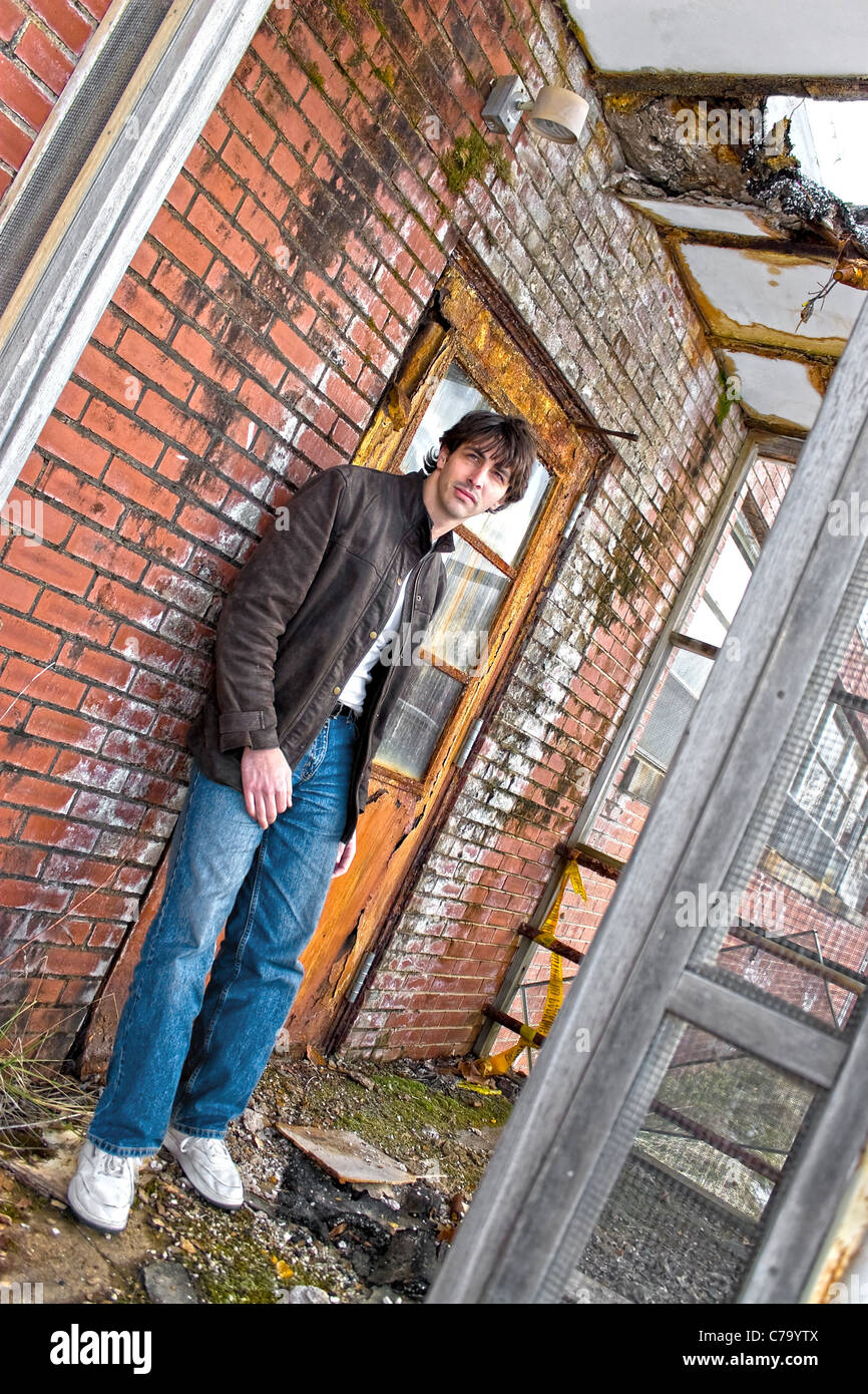 A young brunette man posing outside a worn and abandoned building. Stock Photo