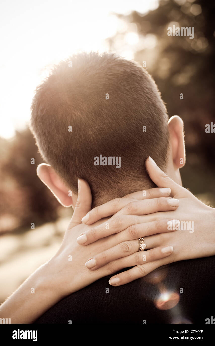 A woman hugs her fiance by placing her hands around his neck in sepia tone. Shallow depth of