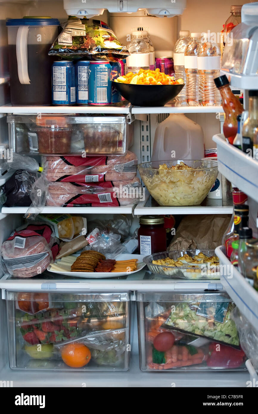 An open refrigerator door showing a full stocked fridge loaded up with food and fresh ingredients. Stock Photo