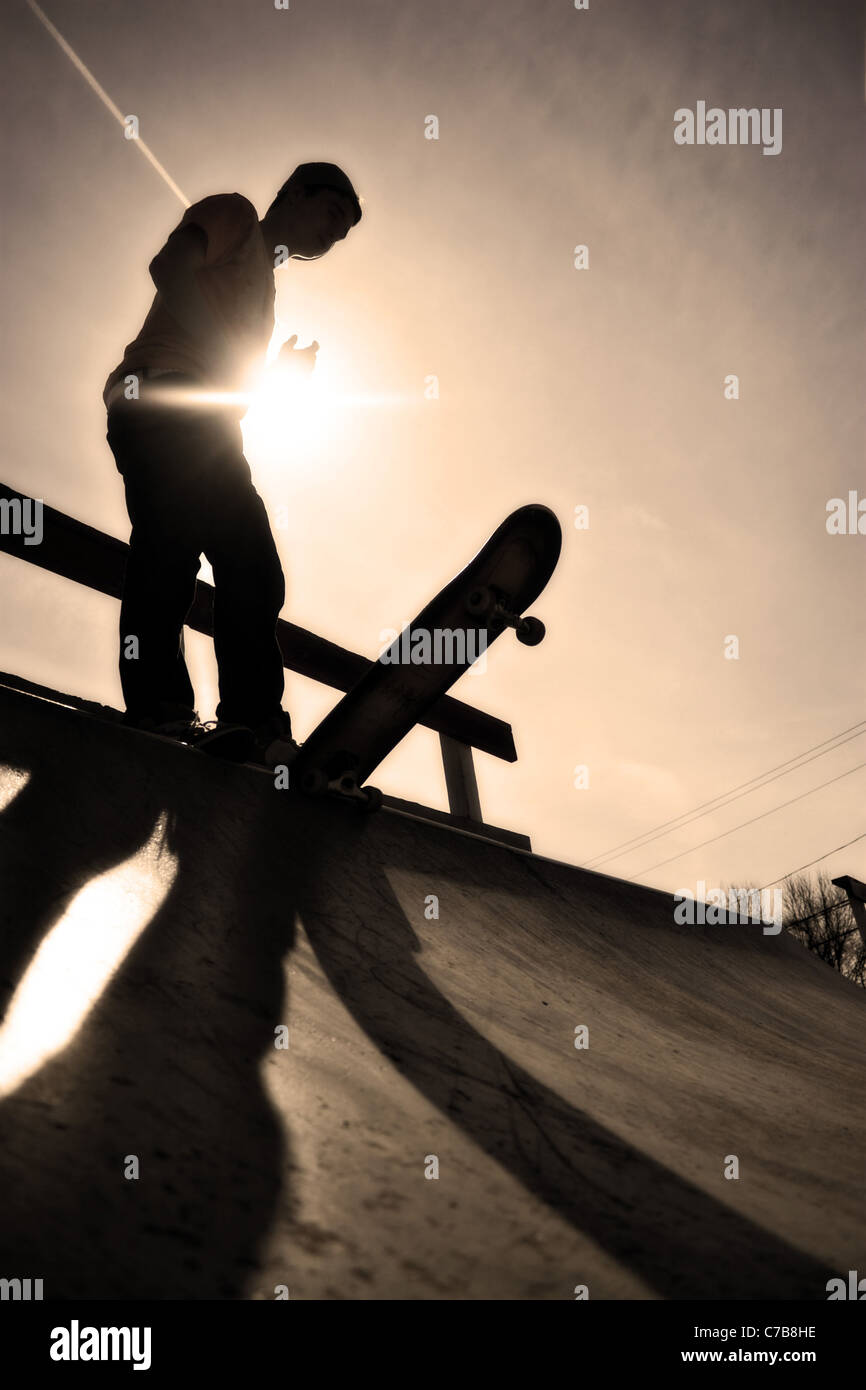 Silhouette of a young skateboarder at the top of the ramp. Stock Photo