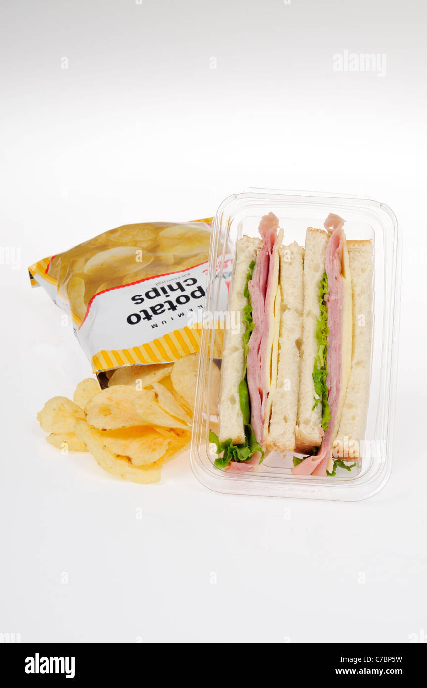 Ham salad with cheese sandwich takeaway with lettuce on white bread in plastic packet container and bag of crisps on white. Stock Photo