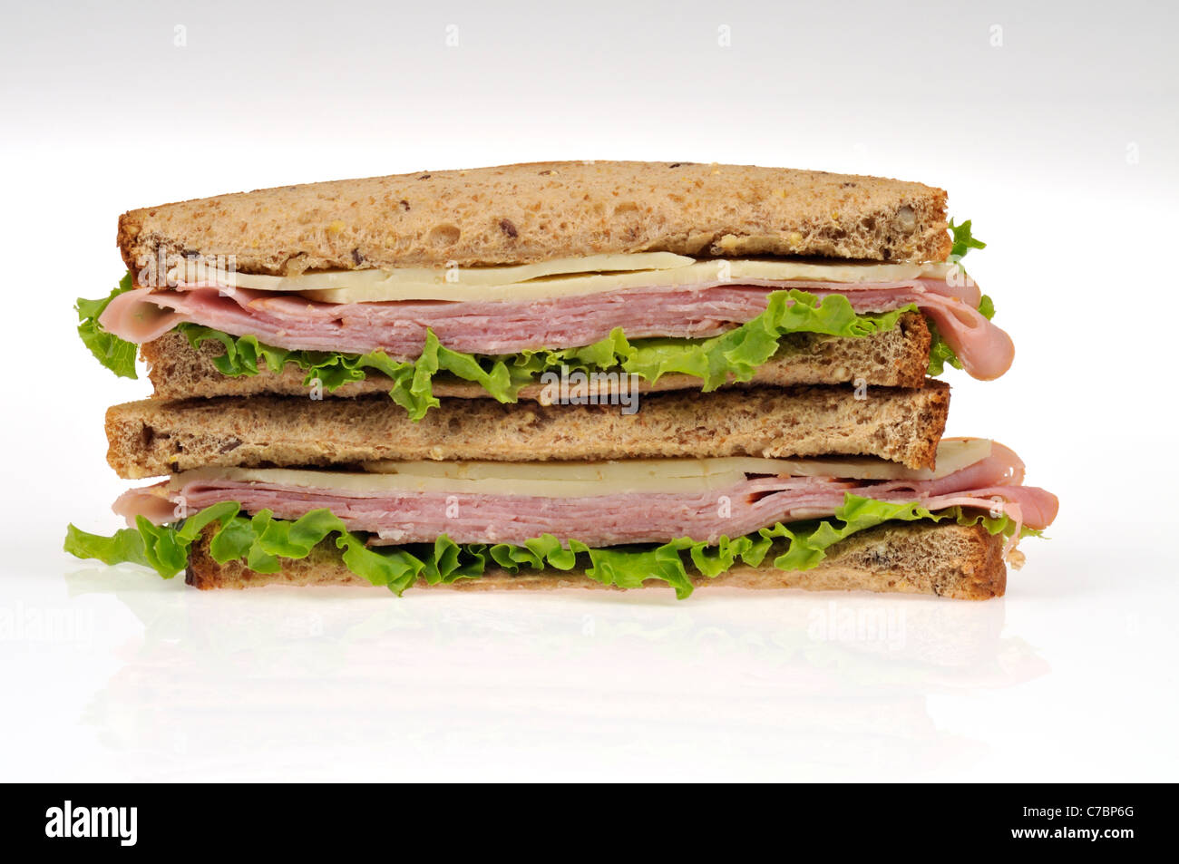 Halves of a ham and cheese sandwich on whole meal bread with lettuce stacked on white background, isolated. Stock Photo