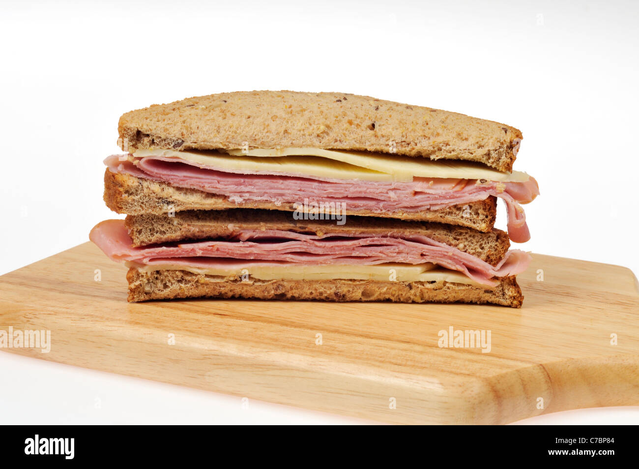 Ham and cheese sandwich on whole meal bread cut in half on wood cutting board on white background. Stock Photo