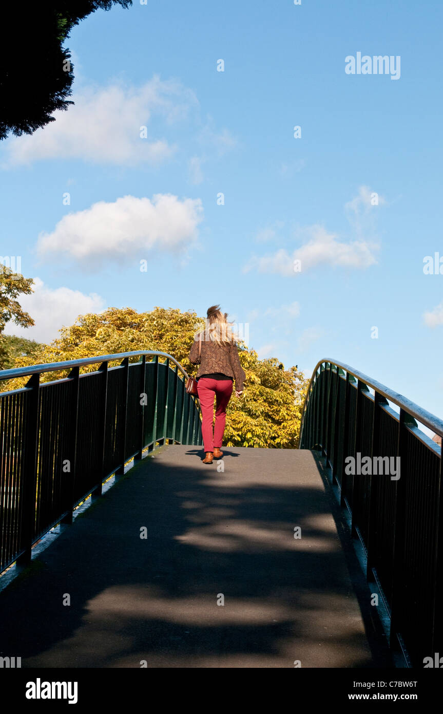 Woman in red trousers crossing the Eel Pie Island pedestrian bridge, Twickenham, Middlesex, England, United Kingdom Stock Photo