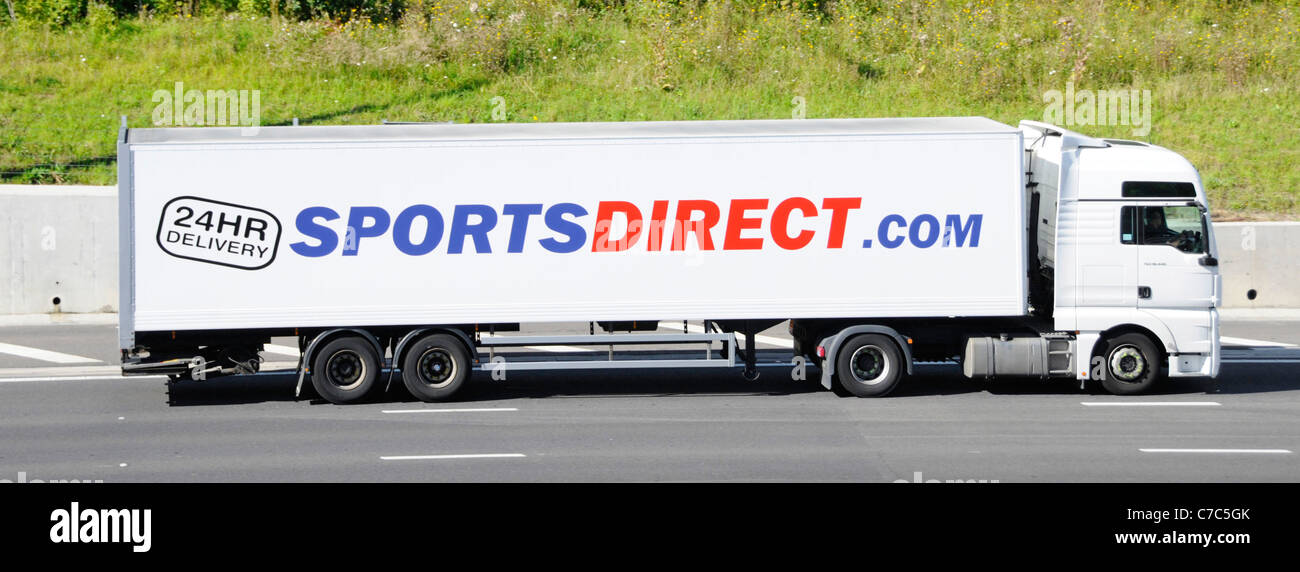 Sports Direct internet site advertising on side of long supply chain articulated delivery trailer & white hgv lorry truck driving on UK motorway Stock Photo