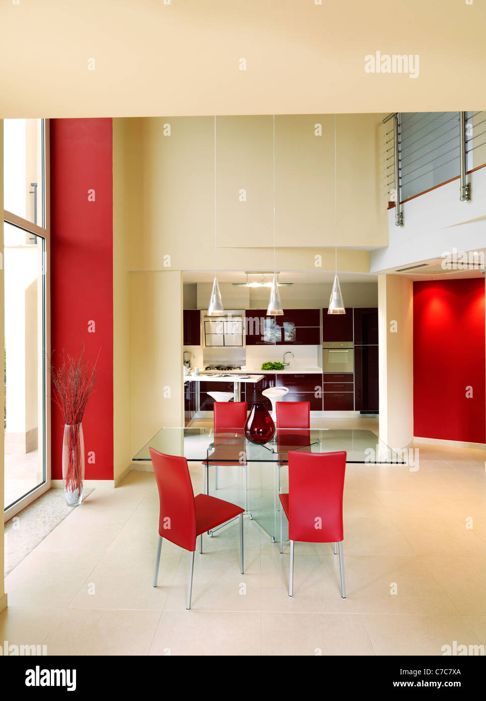 modern dining room with kitchen view and glass table around four red chairs Stock Photo